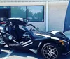 A person is seated in a parked Polaris Slingshot three-wheeled vehicle smiling and holding the steering wheel