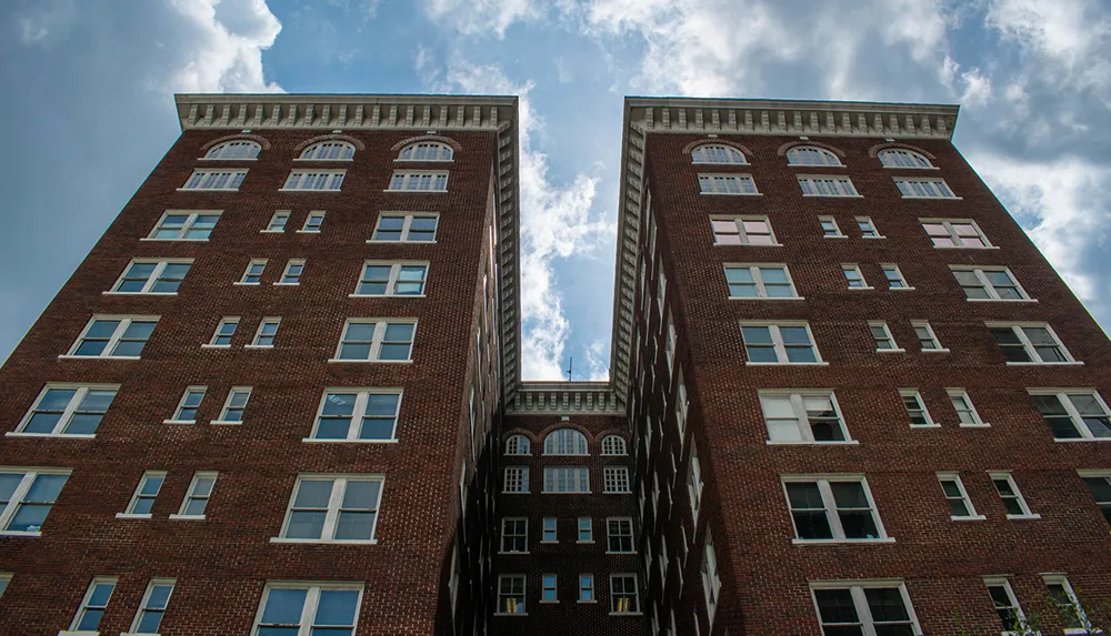 Two symmetric red-brick high-rise buildings converge towards a blue sky with wispy clouds