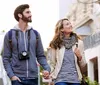 A smiling couple with the man carrying a camera holds hands while walking and gazing around in an urban setting during what appears to be dusk