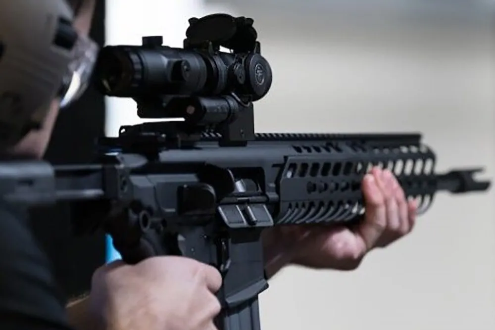 A person is aiming a rifle equipped with a scope focusing on the view from the rear of the weapon