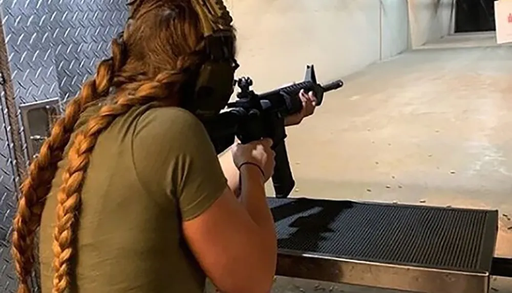 A person with a long braid is aiming a rifle at a target on a shooting range