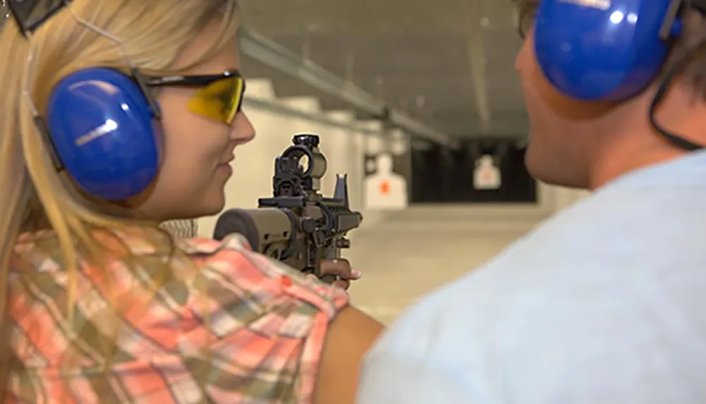 A woman is aiming a rifle at a shooting range under the supervision of an instructor