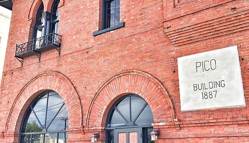 This image shows the facade of the red-brick Pico Building constructed in 1887 featuring arched windows and a balcony