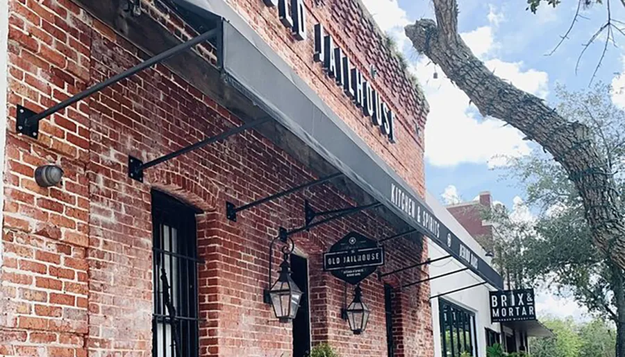 This image shows the exterior of a brick building with signage indicating a place called BRIX & MORTAR, framed under a large tree branch with clear skies in the background.