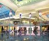 The image shows a dusk view of a stylish modern shopping mall entrance flanked by palm trees and featuring upscale storefronts