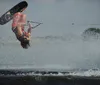 A person is performing a water skiing trick holding onto a handle with a rope while leaning back and creating a splash on the water