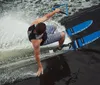 A person is performing a water skiing trick holding onto a handle with a rope while leaning back and creating a splash on the water