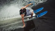 A person is performing a water skiing trick, holding onto a handle with a rope while leaning back and creating a splash on the water.