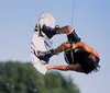 A person is performing a water skiing trick holding onto a handle with a rope while leaning back and creating a splash on the water