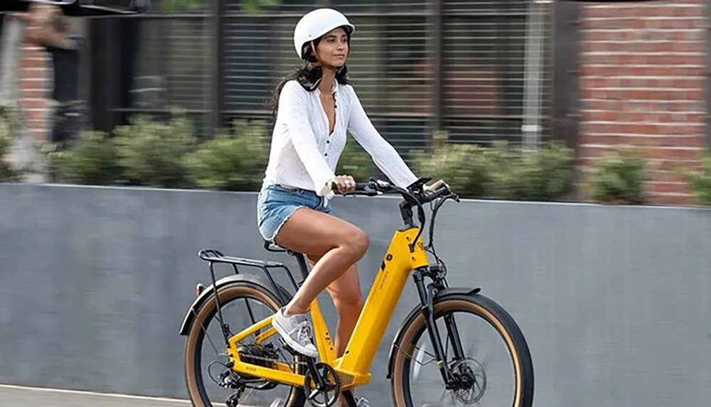 A person is riding a yellow electric bicycle on the street wearing a white helmet and casual clothing