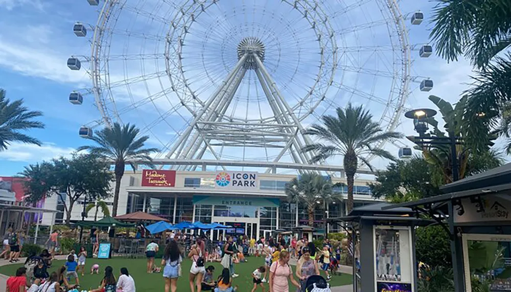 Visitors are enjoying a sunny day at a lively entertainment complex with a large Ferris wheel dominating the skyline