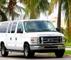 A white Ford passenger van is driving on a road lined with palm trees