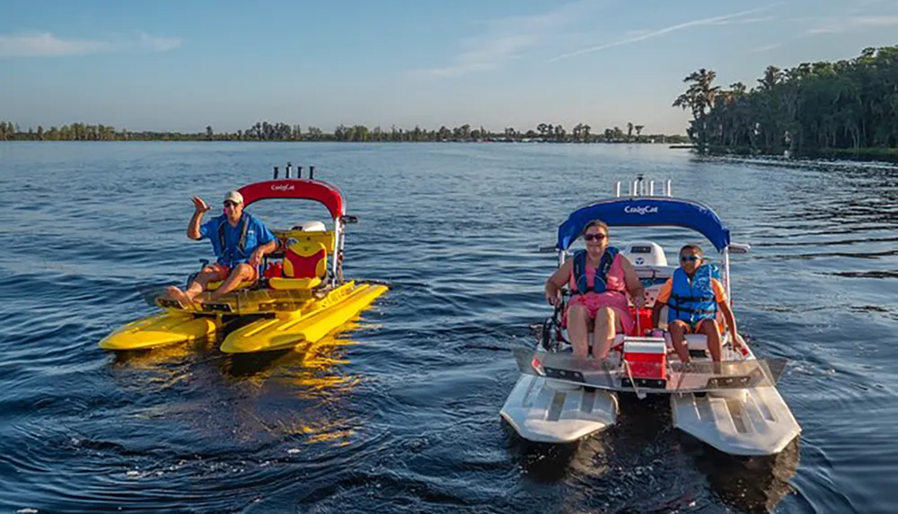 Three people are enjoying a sunny day on the water with two unique small watercraft against a backdrop of trees and open sky