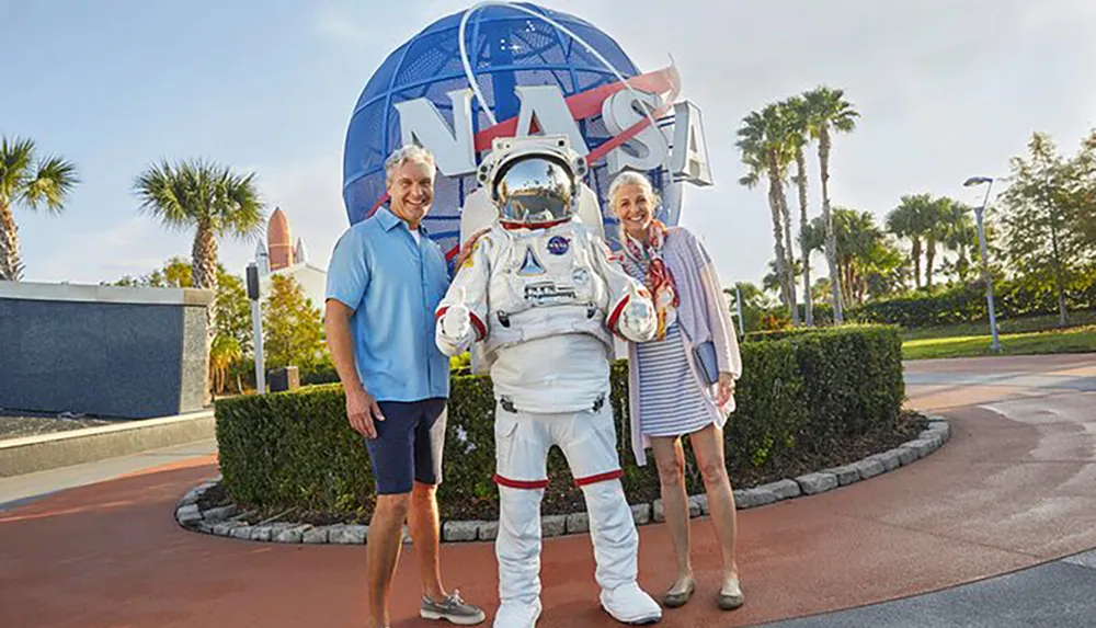 Two people are posing for a photo with a person in a NASA spacesuit in front of a large NASA logo