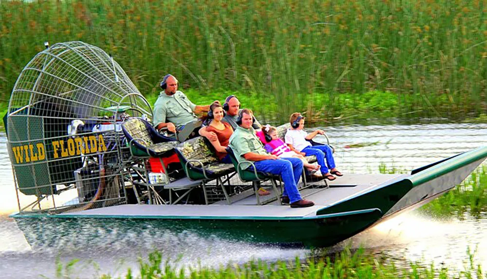 A group of people is enjoying a ride on a large airboat through a grassy wetland area