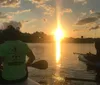 Two individuals are smiling while kayaking in an urban waterway at dusk with city lights starting to twinkle in the background