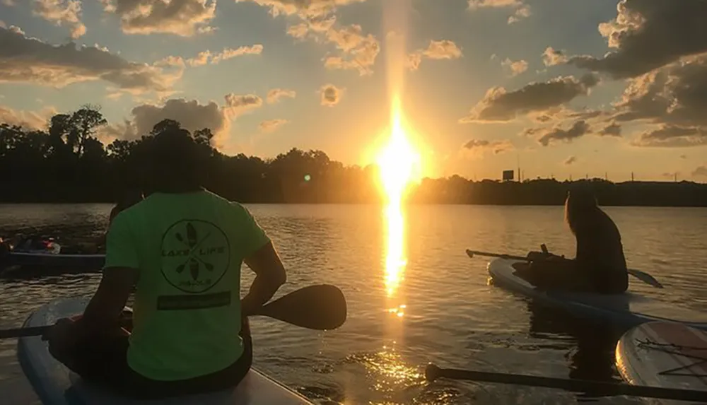 Two individuals are kayaking on calm waters against the backdrop of a stunning sunset