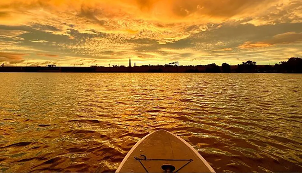 A kayak bows towards a vibrant golden sunset over a rippling body of water creating a serene and picturesque scene