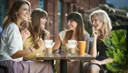 Four women are enjoying a lively conversation at an outdoor café table with beverages.
