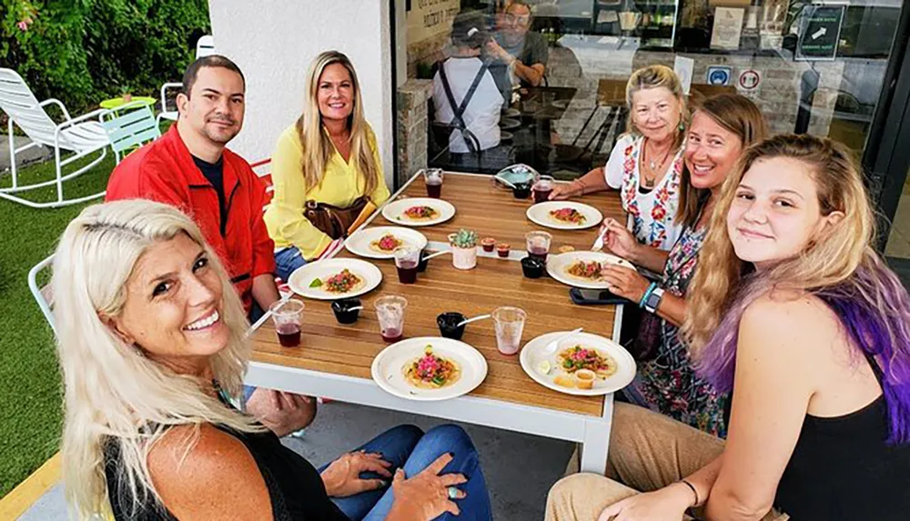 A group of individuals is joyfully dining outdoors at a table with various dishes and drinks in front of them