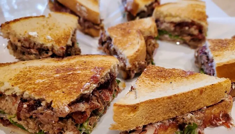 The image shows several toasted sandwiches cut into halves filled with meat and other ingredients on a white paper-lined tray