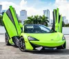 A bright green sports car with its doors open upwards is parked with a backdrop of high-rise buildings under a blue sky