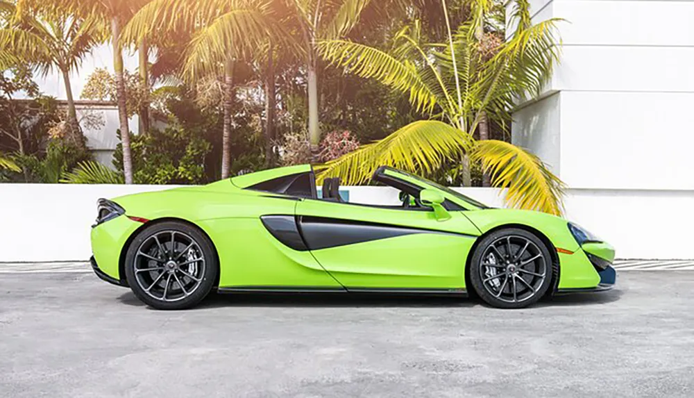 A bright green sports car is parked outdoors near palm trees and a white building