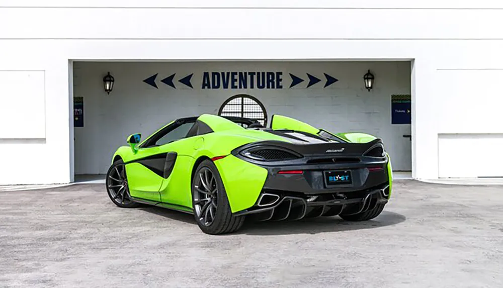 A bright green sports car is parked in front of a garage with the word ADVENTURE above the entrance