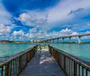 A dolphin is energetically leaping out of the water near a bridge under a partly cloudy sky