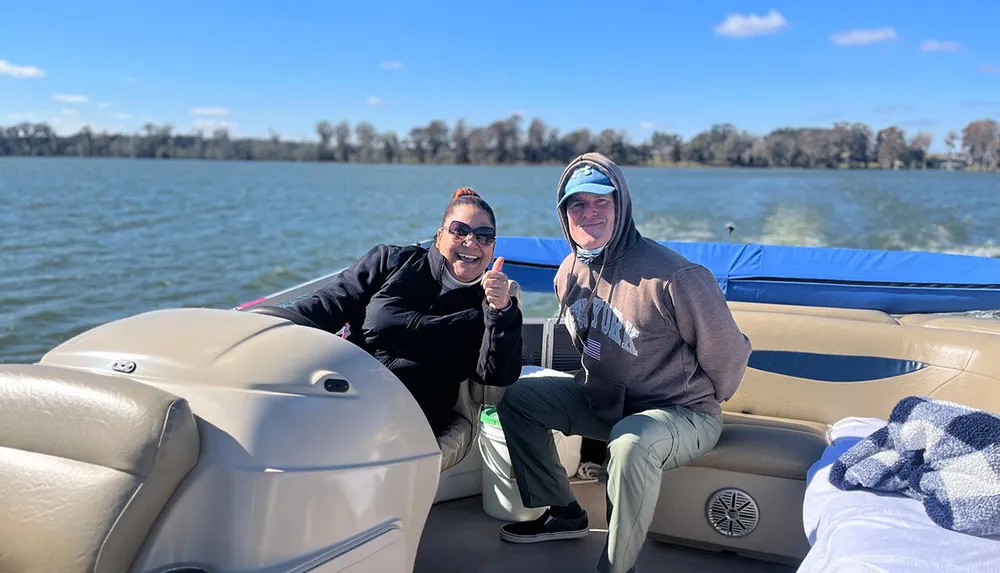Two people are smiling and posing for a photo while enjoying a boat ride on a sunny day