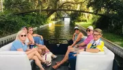 A group of people is enjoying a boat ride on a tree-lined canal.