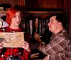 A woman and a man are in a dimly lit vintage-style room where the woman appears concerned while holding a newspaper with the headline KILLER ON THE LOOSE as the man points to something possibly providing an explanation