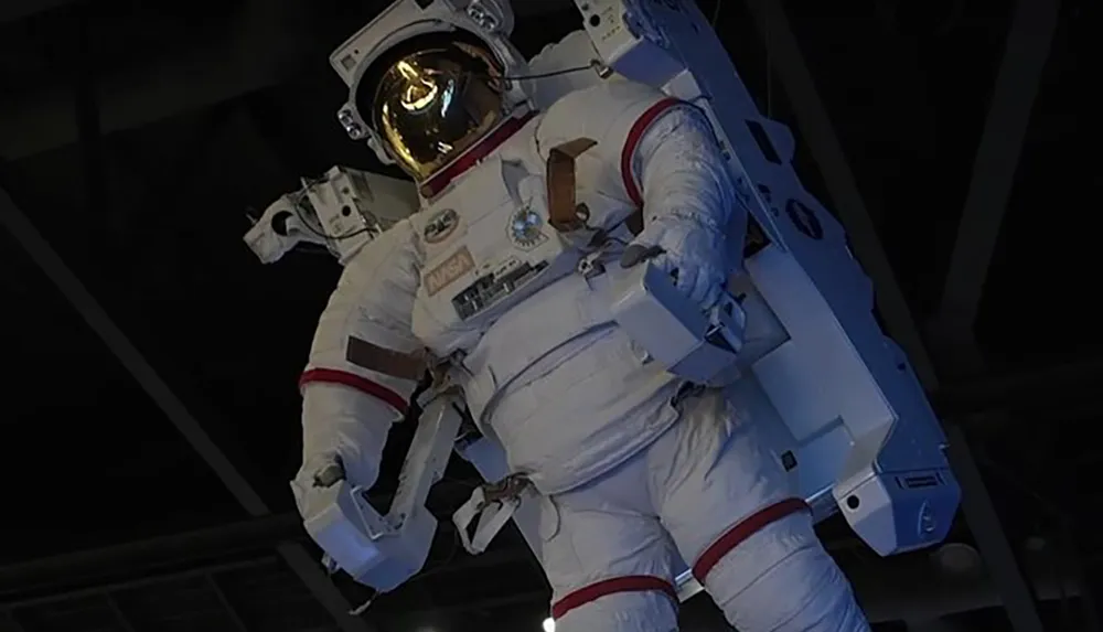 This image shows a person in a white NASA spacesuit with a golden visor helmet potentially on display or during an activity simulating space conditions
