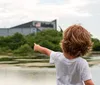 A child with curly hair seen from behind is pointing towards a rocket or space shuttle displayed near a building with Atlantis written on it suggesting the setting may be a space exploration exhibit or museum