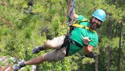 A man wearing a helmet and harness is enjoying a zipline ride through a forest.