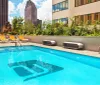 A rooftop swimming pool surrounded by lounge chairs basks in sunlight amidst urban skyscrapers