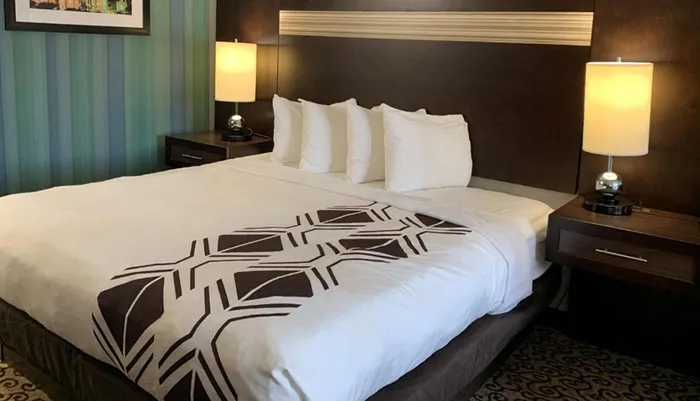 The image shows a neatly made bed with a geometric-patterned comforter in a well-appointed hotel room