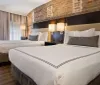 The image shows a modern hotel room with two neatly made queen-size beds brick wall accents and soft lighting creating a cozy and inviting atmosphere
