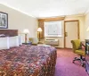 The image shows a basic hotel room with a patterned bedspread two lamps a framed picture on the wall a CRT television and simple furnishings
