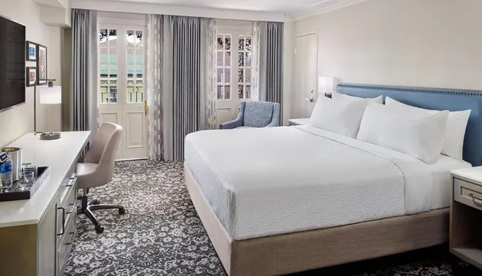 The image shows a well-appointed hotel room with a large bed a desk area and French doors leading to a balcony