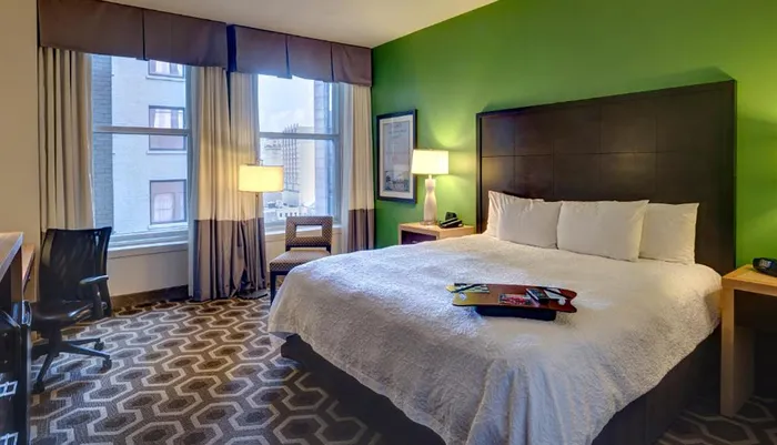 This image shows a modern hotel room with a bed desk chair and a bright green accent wall