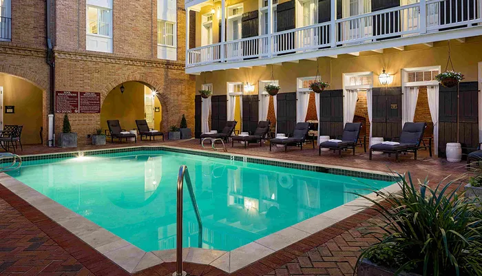 A tranquil evening at a courtyard pool surrounded by a brick building with loungers and decorative plants displaying an inviting and cozy atmosphere