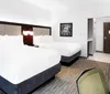 This image shows a modern and neatly arranged hotel room with two queen-sized beds clean white linens a wall-mounted art piece and a glimpse of the entrance area