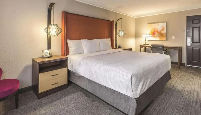 The image shows a well-appointed modern hotel room with a large bed a desk and contemporary furnishings