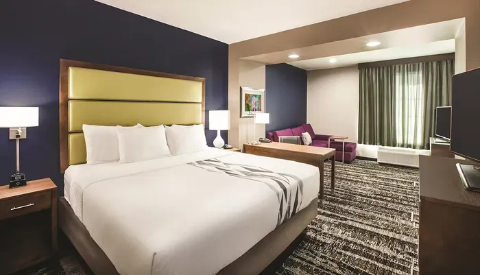 The image shows a modern hotel room with a large bed a seating area and contemporary decor