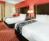 The image shows a neatly arranged hotel room with two queen-sized beds featuring a red and black color scheme and a striped carpet