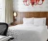 The image presents a modern and stylish hotel room with an artistic red chandelier a patterned bedspread wooden headboard and tasteful decor