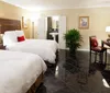 The image shows a neatly arranged double bedroom with two beds white linens red accent pillows and traditional decor