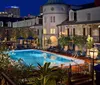 The image shows a serene nocturnal poolside setting with surrounding lounge areas illuminated by ambient lighting located amidst traditional architectural buildings likely from a hotel or resort