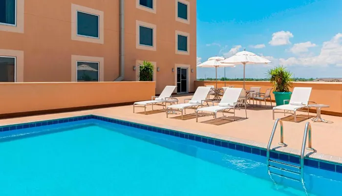 A sunny hotel pool deck with lounge chairs and umbrellas awaits guests for a relaxing day outdoors